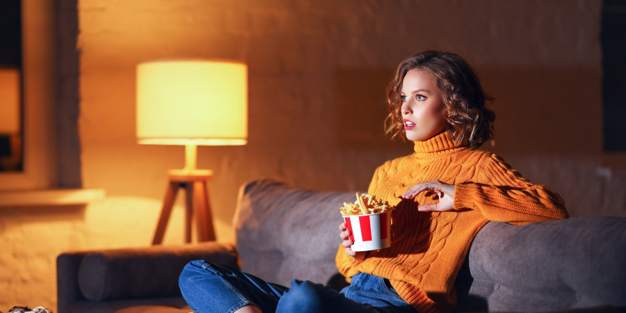 Une jeune femme sur son sofa en train de visionner un contenu culturel dématérialisé de type vidéo.