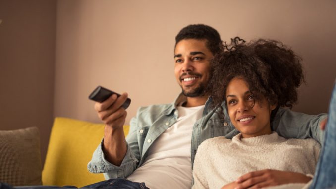 Un couple installé dans un sofa visionnant un contenu vidéo, dont l’audience est ou sera mesurée par Médiamétrie.