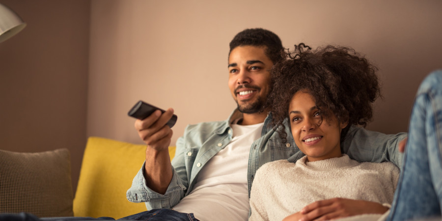 Un couple installé dans un sofa visionnant un contenu vidéo, dont l’audience est ou sera mesurée par Médiamétrie.