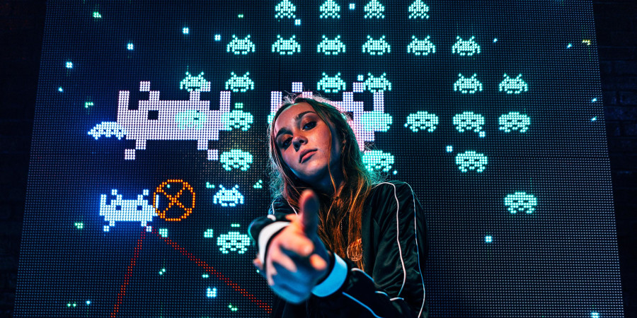 La DJ Mariana BO ayant travaillé avec le label Beat Drop postée devant l’écran d’une version du jeu Space invaders