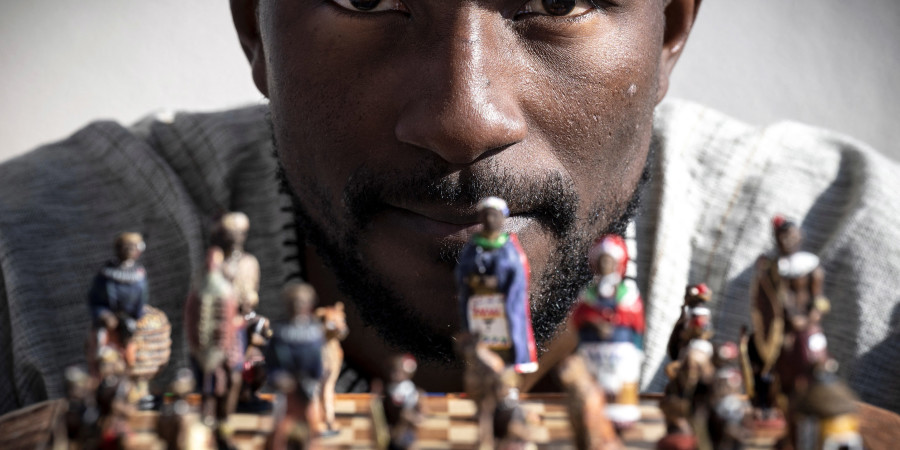 Teddy Kossoko, assis devant un jeu d’échecs avec des pions à l’effigie de personnages africains.