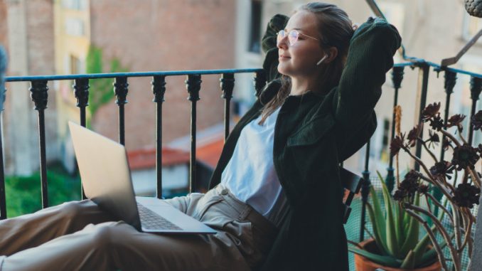 Une femme avec son PC portable en train de travailler sur le balcon d’un hôtel, une parmi les innombrables « digital nomads » voyageant à travers l’Europe.