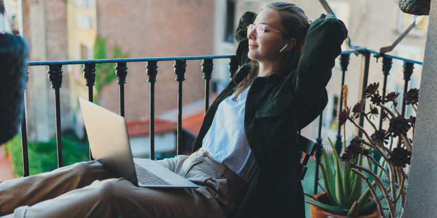 Une femme avec son PC portable en train de travailler sur le balcon d’un hôtel, une parmi les innombrables « digital nomads » voyageant à travers l’Europe.