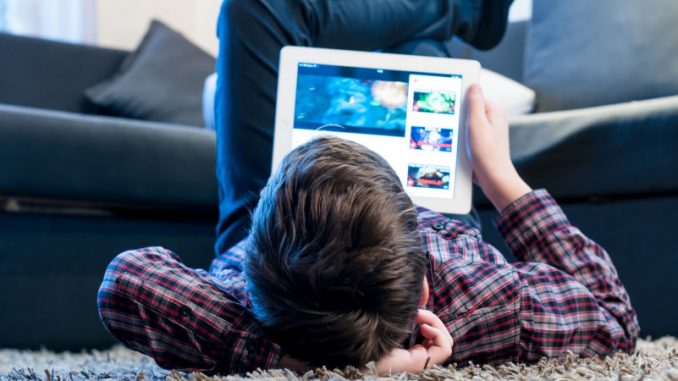 Un jeune garçon en train de regarder sa tablette dans son salon, expérimentant les effets des jeux vidéo sur le cerveau ainsi que des écrans.