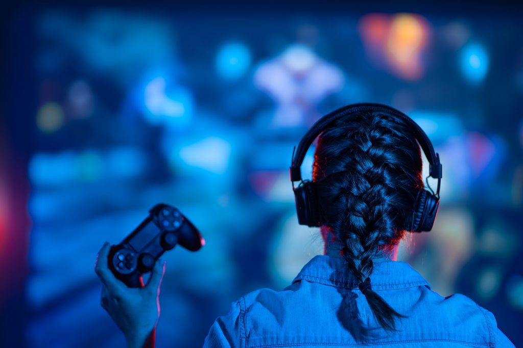 Une jeune femme jouant a des jeux video : manette a la main et casque aux oreilles