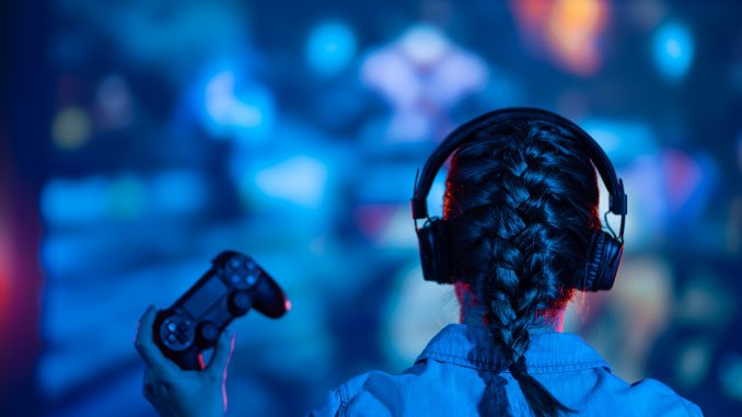 Une jeune femme jouant a des jeux video : manette a la main et casque aux oreilles