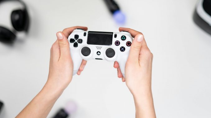 Un joueur tenant une manette de PlayStation grise dans ses mains.