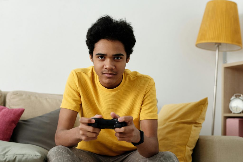 Un jeune adolescent assis sur un concentré, manette à la main, concentré sur son jeu vidéo.