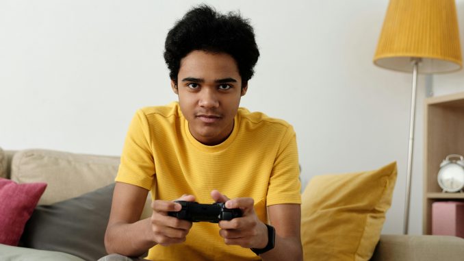 Un jeune adolescent assis sur un concentré, manette à la main, concentré sur son jeu vidéo.