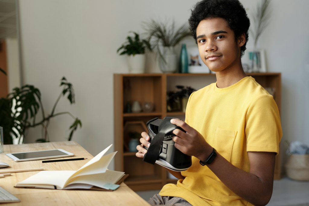 Assis devant une table, un jeune adolescent tient un casque VR, un équipement mis en avant dans les bibliothèques 4.0.