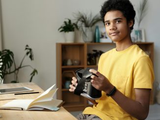 Assis devant une table, un jeune adolescent tient un casque VR, un équipement mis en avant dans les bibliothèques 4.0.