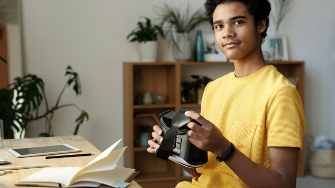 Assis devant une table, un jeune adolescent tient un casque VR, un équipement mis en avant dans les bibliothèques 4.0.